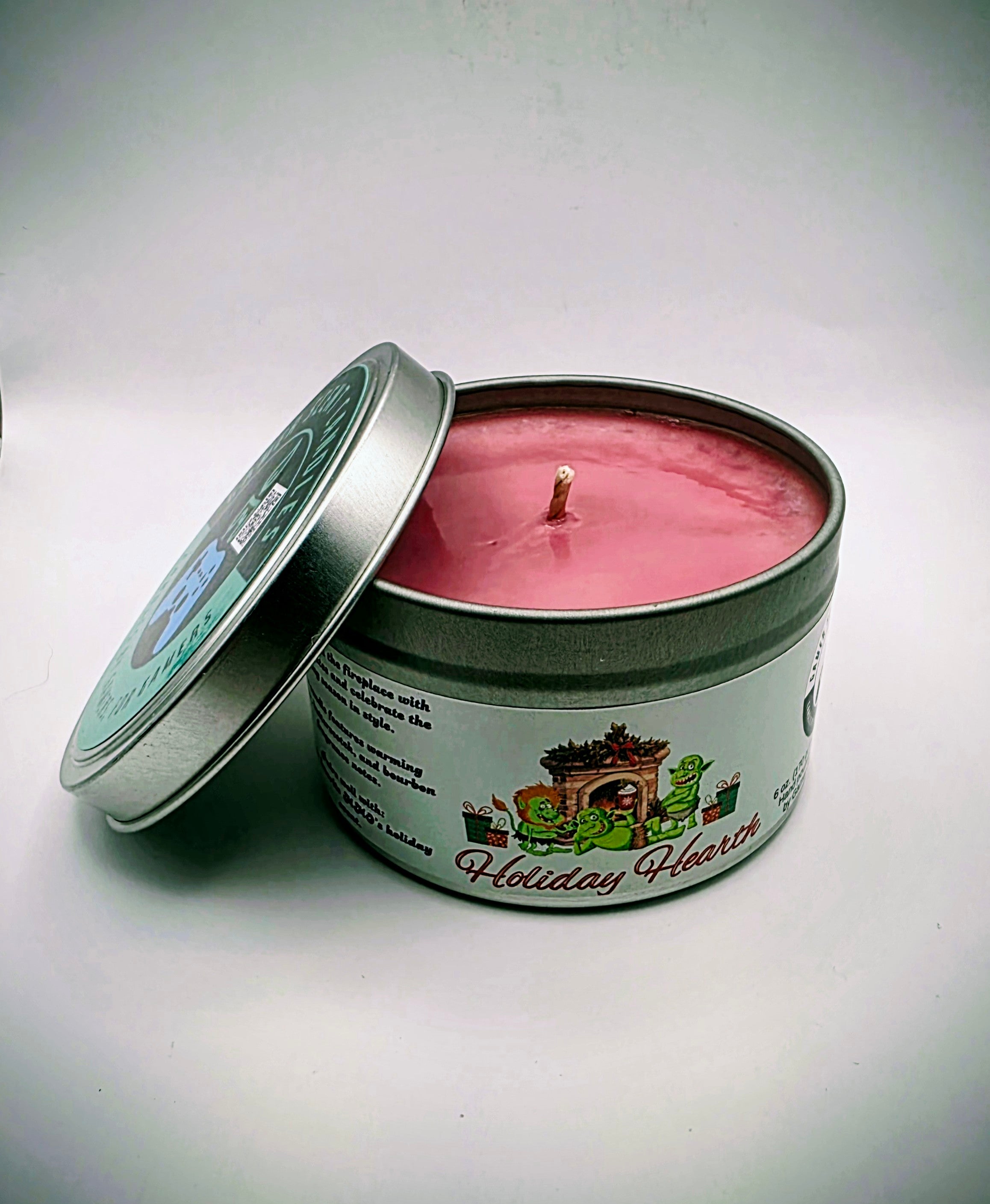 A 6 oz. candle in a candle tin named "Holiday Hearth" featuring a festive gathering of orcs around a fireplace during the holiday season.