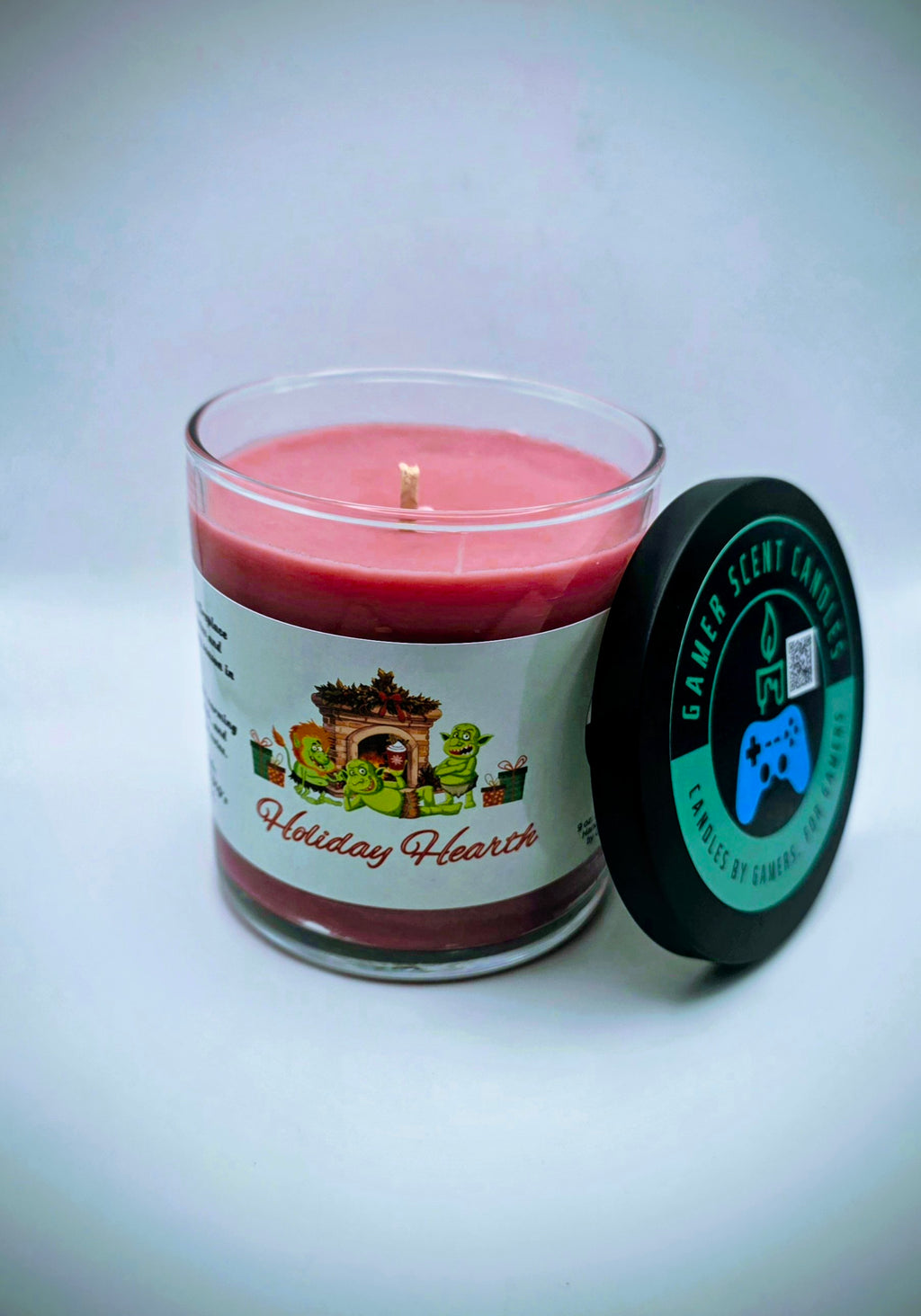 A 9 oz. candle in a glass tumbler jar named "Holiday Hearth". The label features a festive gathering of orcs around a fireplace during the holiday season.