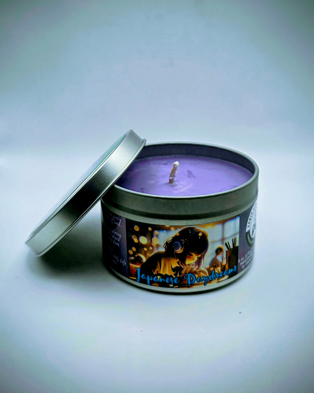 Our "Japanese Daydreams" candle in a 6 oz. tin. The candle features Sakura (cherry blossom) and plum fragrance notes. The candle is purple and features a purple label with a young Japanese girl wearing headphones, daydreaming during class. Our 6 oz. candles have approximately a 25 hour burn time.