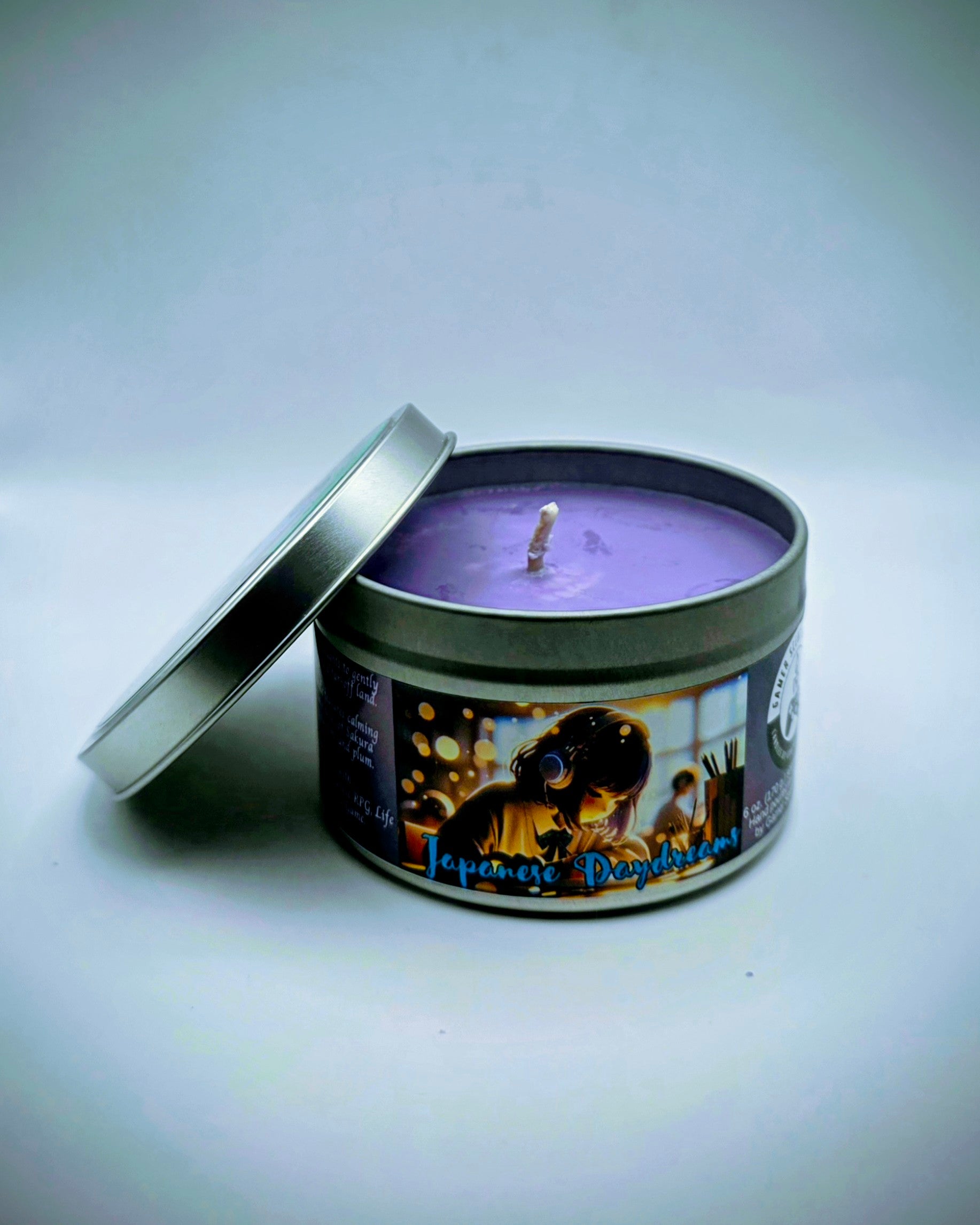 Our "Japanese Daydreams" candle in a 6 oz. tin. The candle features Sakura (cherry blossom) and plum fragrance notes. The candle is purple and features a purple label with a young Japanese girl wearing headphones, daydreaming during class. Our 6 oz. candles have approximately a 25 hour burn time.
