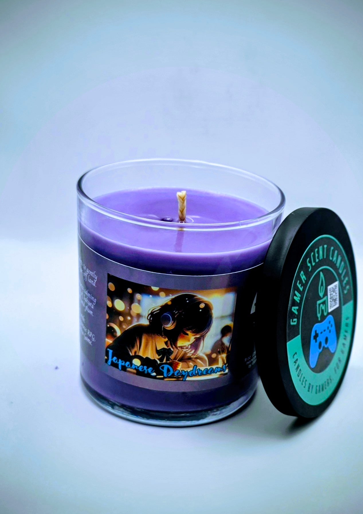 Our "Japanese Daydreams" candle in a 9 oz. glass tumbler jar. The candle features Sakura (cherry blossom) and plum fragrance notes. The candle is purple and features a purple label with a young Japanese girl wearing headphones, daydreaming during class. Our 9 oz. candles have approximately a 40 hour burn time.