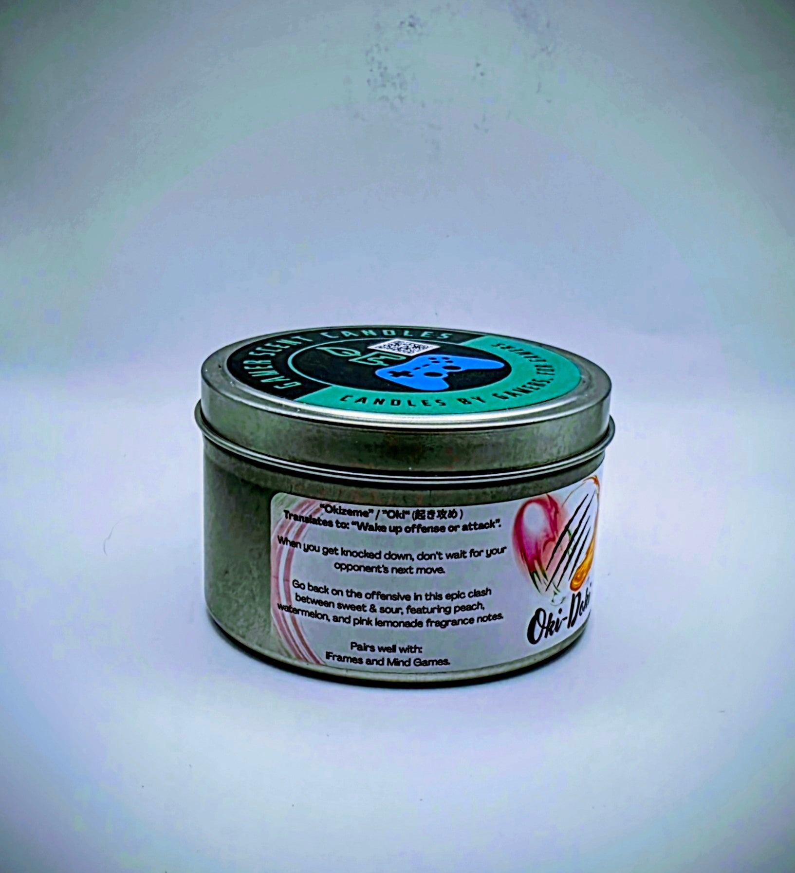 Our Oki-Doki candle in a candle tin. It has a net weight of 6 oz. and approximately a 25 hour burn time. It features a mixture of sweet and sour fragrance notes including peach, watermelon, and pink lemonade. The clash between sweet and sour is meant to represent the clash between powerful fighters in your favorite fighting game franchises. The label is white with images reminiscent of the fireball and slashing attacks featured in many fighting games.
