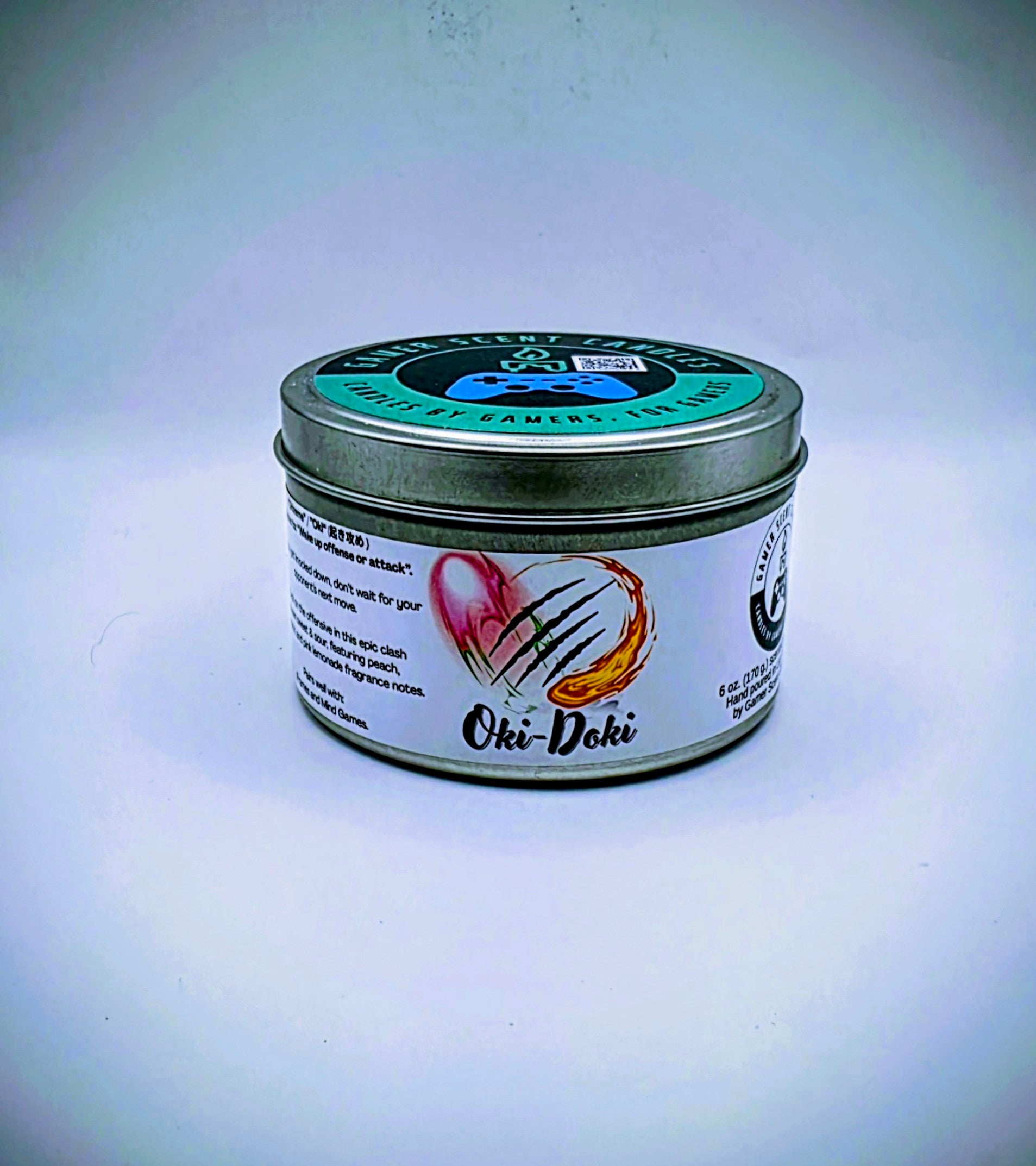 Our Oki-Doki candle in a candle tin. It has a net weight of 6 oz. and approximately a 25 hour burn time. It features a mixture of sweet and sour fragrance notes including peach, watermelon, and pink lemonade. The clash between sweet and sour is meant to represent the clash between powerful fighters in your favorite fighting game franchises. The label is white with images reminiscent of the fireball and slashing attacks featured in many fighting games.