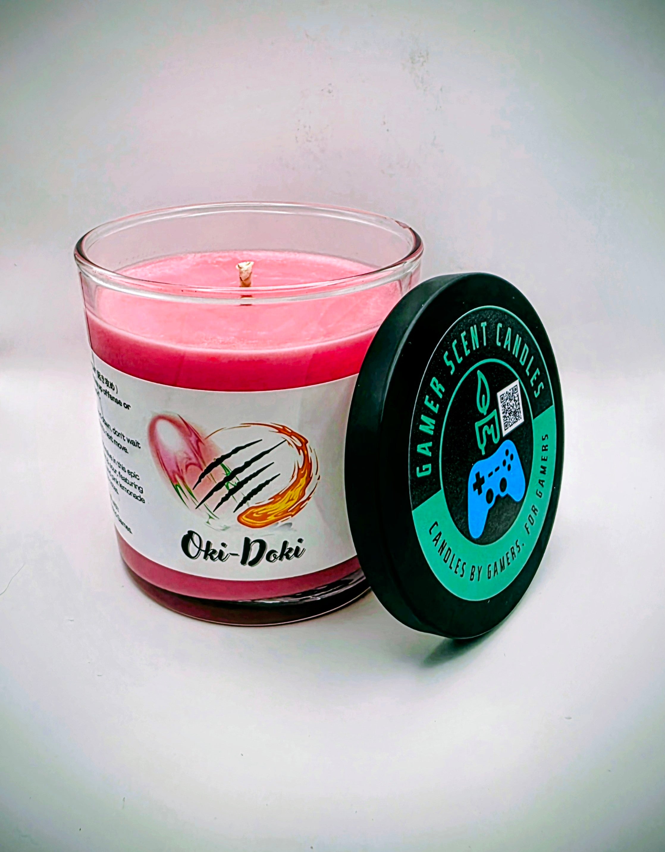 Our Oki-Doki candle in a glass tumbler jar. It has a net weight of 9 oz. and approximately a 40 hour burn time. It features a mixture of sweet and sour fragrance notes including peach, watermelon, and pink lemonade. The clash between sweet and sour is meant to represent the clash between powerful fighters in your favorite fighting game franchises. The label is white with images reminiscent of the fireball and slashing attacks featured in many fighting games.