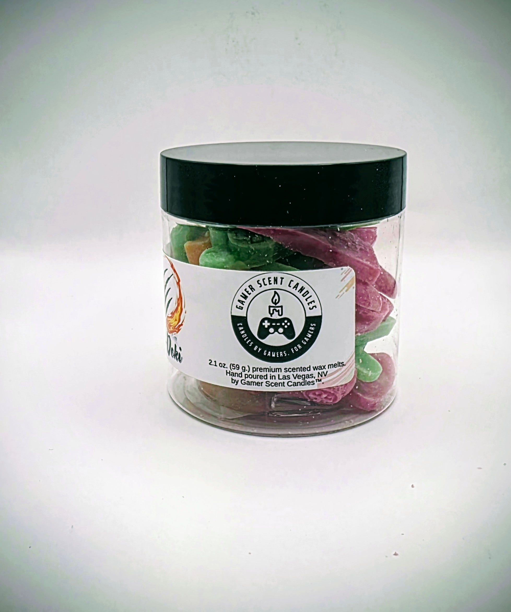 A jar of "Oki-Doki" premium wax melts. The wax melts come in a clear plastic jar, with a white label, featuring imagery reminiscent of fighting games. The wax melts come in a variety of video game controller shapes, and a mix of orange, green, and pink colors.