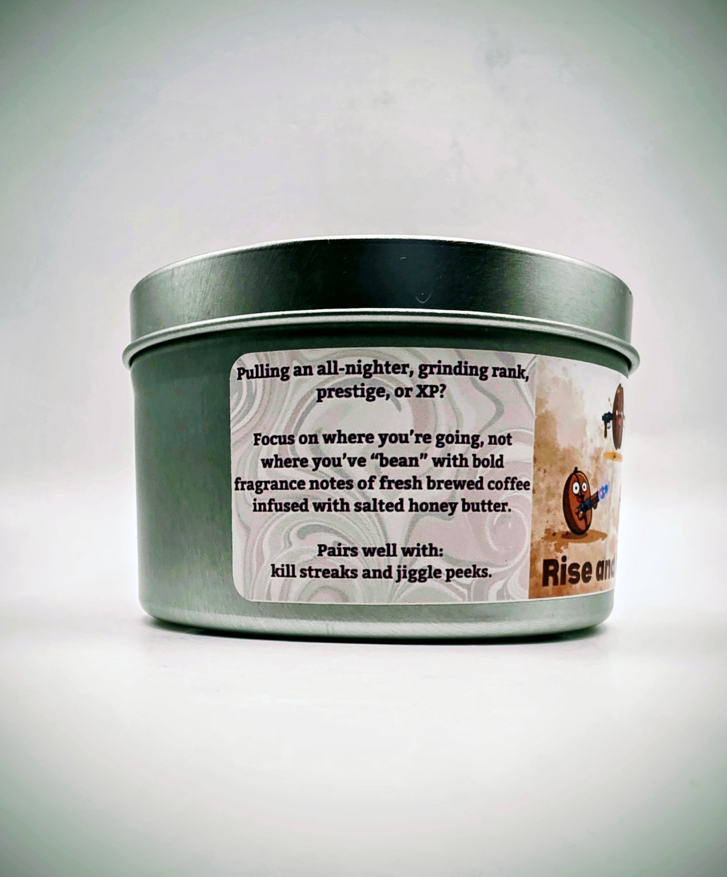 Our "Rise and Grind" fragrance in a 6 oz. tin. It features bold fragrance notes of fresh brewed coffee infused with salted honey butter. Our 6 oz. tins have approximately a 25 hour burn time. The label features cartoon coffee beans with weapons.
