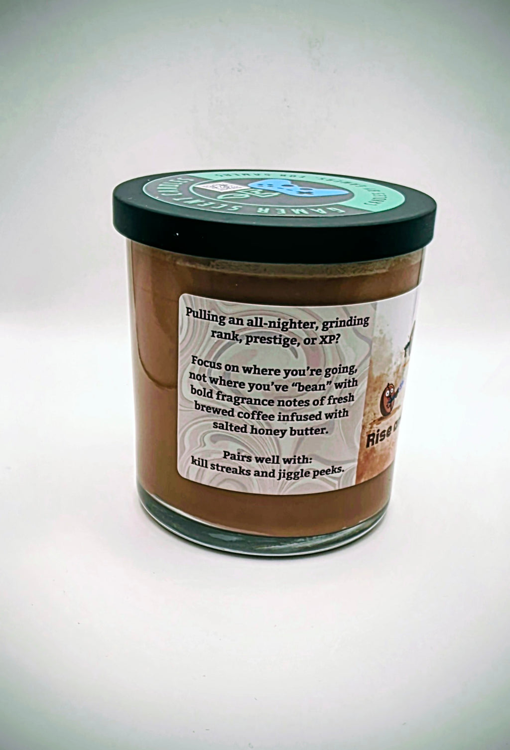 Our "Rise and Grind" fragrance in a 9 oz. glass tumbler jar with black lid. It features bold fragrance notes of fresh brewed coffee infused with salted honey butter. Our 9 oz. jars have approximately a 40 hour burn time. The label features cartoon coffee beans with weapons.