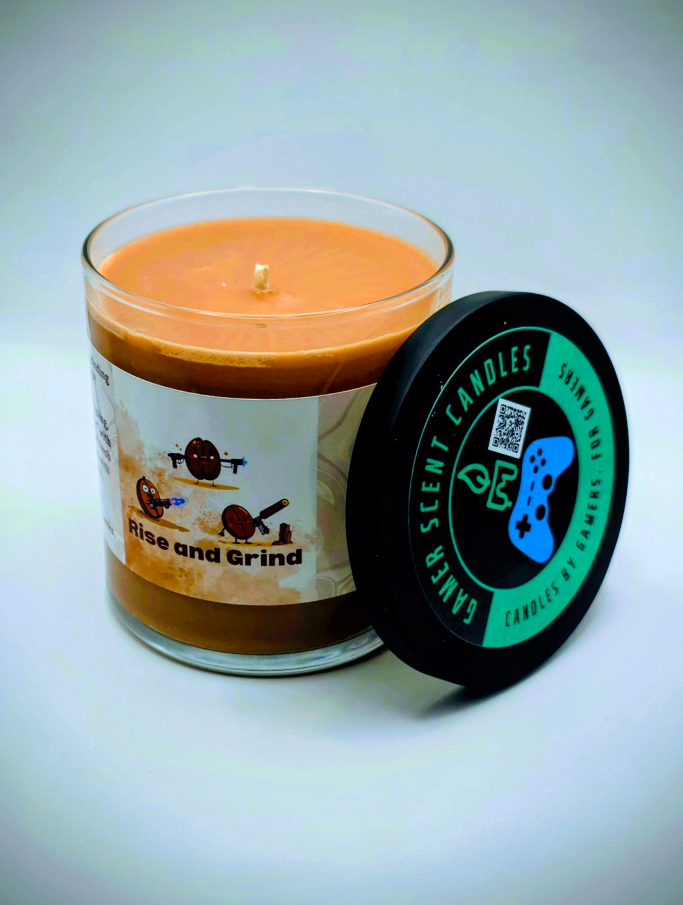 Our "Rise and Grind" fragrance in a 9 oz. glass tumbler jar with black lid. It features bold fragrance notes of fresh brewed coffee infused with salted honey butter. Our 9 oz. jars have approximately a 40 hour burn time. The label features cartoon coffee beans with weapons.