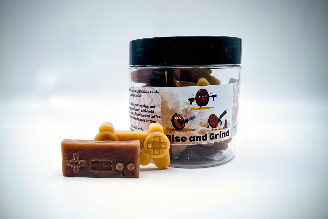 A jar of premium wax melts in an assortment of video game controller shapes. The scent is called "Rise and Grind". The wax melts are a mix of coffee brown and golden cream colors. The label features cartoon coffee beans with weapons.