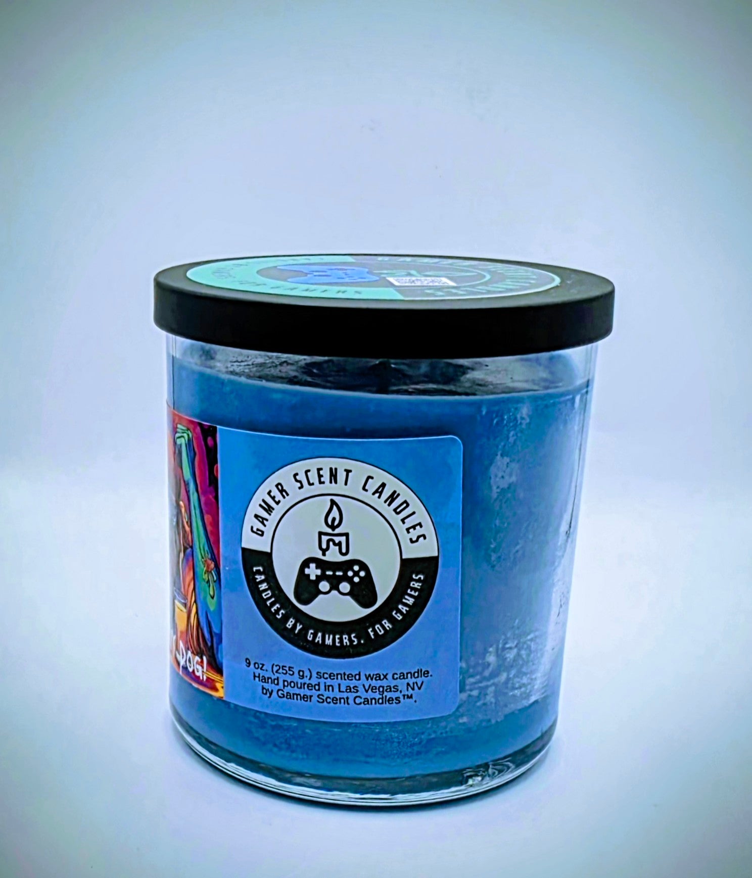 Our "Scurvy Dog" candle in a 9 oz. glass tumbler jar. The candle features spiced coconut and lime fragrance notes. The candle is blue and features a blue label with a psychedelic pirate holding a drink garnished with a lime. Our 9 oz. candles have approximately a 40 hour burn time.