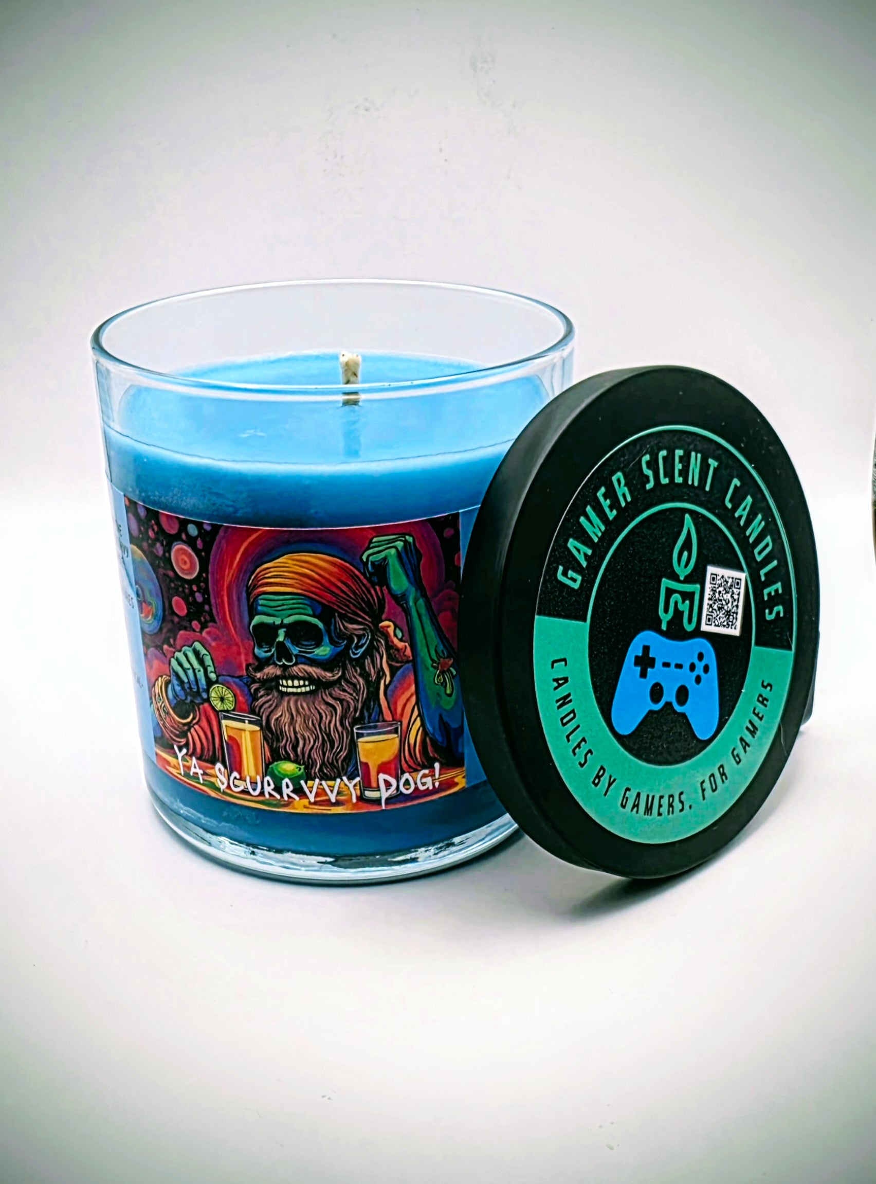 Our "Scurvy Dog" candle in a 9 oz. glass tumbler jar. The candle features spiced coconut and lime fragrance notes. The candle is blue and features a blue label with a psychedelic pirate holding a drink garnished with a lime. Our 9 oz. candles have approximately a 40 hour burn time.