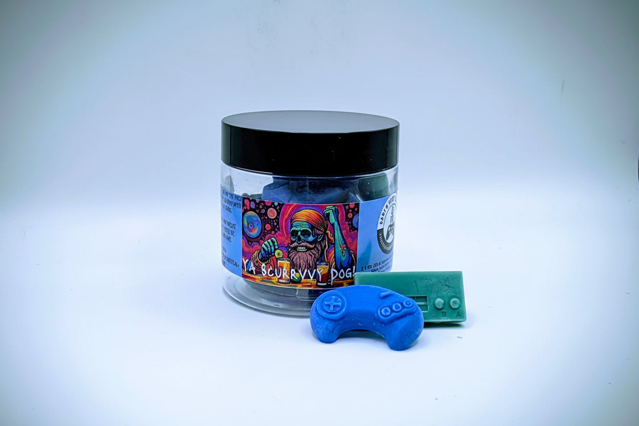 A jar of premium wax melts in an assortment of video game controller shapes. The scent is called "Scurvy Dog". The wax melts are a mix of blue and green colors.  The label features a psychedelic pirate skeleton sitting in front of a beverage garnished with lime.