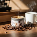 A Rise and Grind 6-ounce candle tin, sitting on a pile of coffee beans, on top of a table, next to a cup of coffee. Front view. Lid off. Lit.  Video game candle. Perfect gift for gamers. Premium soy wax scented candle.