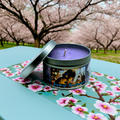 Japanese Daydreams 6-ounce candle tin in front of a field of cherry blossoms. Front view. Lid off. Video game candle for JRPG, Japanese life sim, and gacha games. Perfect gift for gamers.