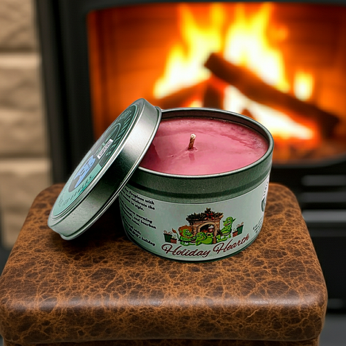 A Holiday Hearth 6-ounce candle tin, sitting on a leather stool in front of a cozy fireplace. Front view. Lid off.  Video game candle. Perfect gift for gamers. Premium soy wax scented candle.