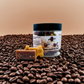 A jar of Rise and Grind premium wax melts, sitting on a pile of coffee beans in front of a light brown background. Lid on. Front view.  Video game wax melts. Perfect gift for gamers. Premium soy wax scented wax melts. Wax tarts.